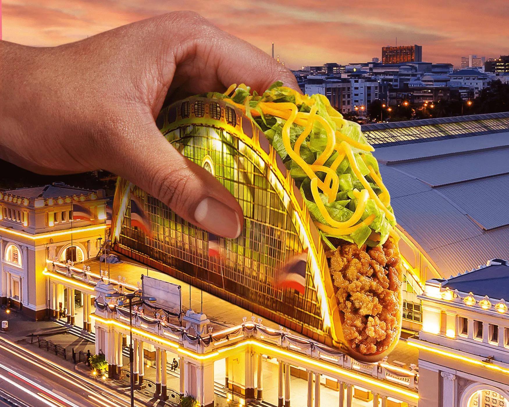 A hand holding a Taco Bell taco built from the Hua Lamphong railway station in Bangkok