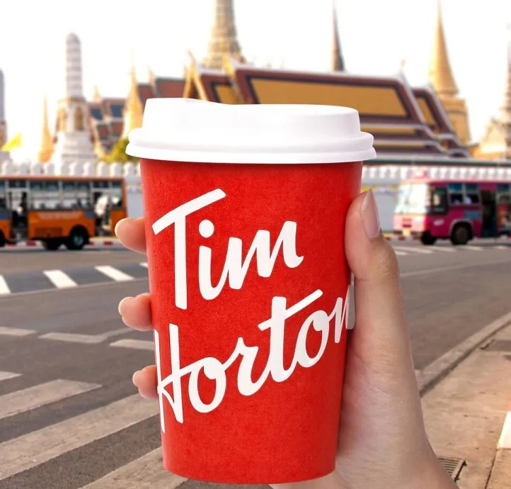A hand holding a Tim Hortons cup in front of a temple in Bangkok