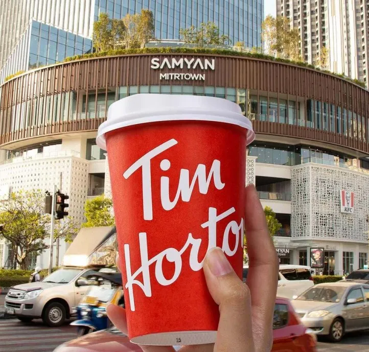 A hand holding a Tim Hortons cup in front of Samyan Mitrtown in Bangkok