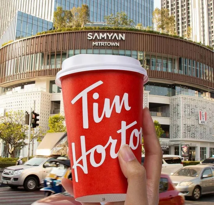 A hand holding a Tim Hortons cup in front of Samyan Mitrtown in Bangkok