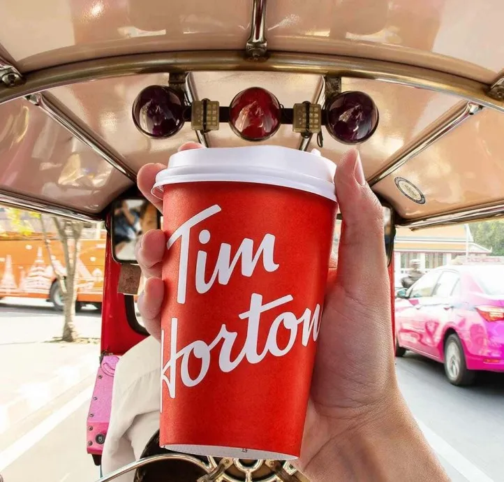 A hand holding a Tim Hortons cup inside a tuk-tuk on a Bangkok street